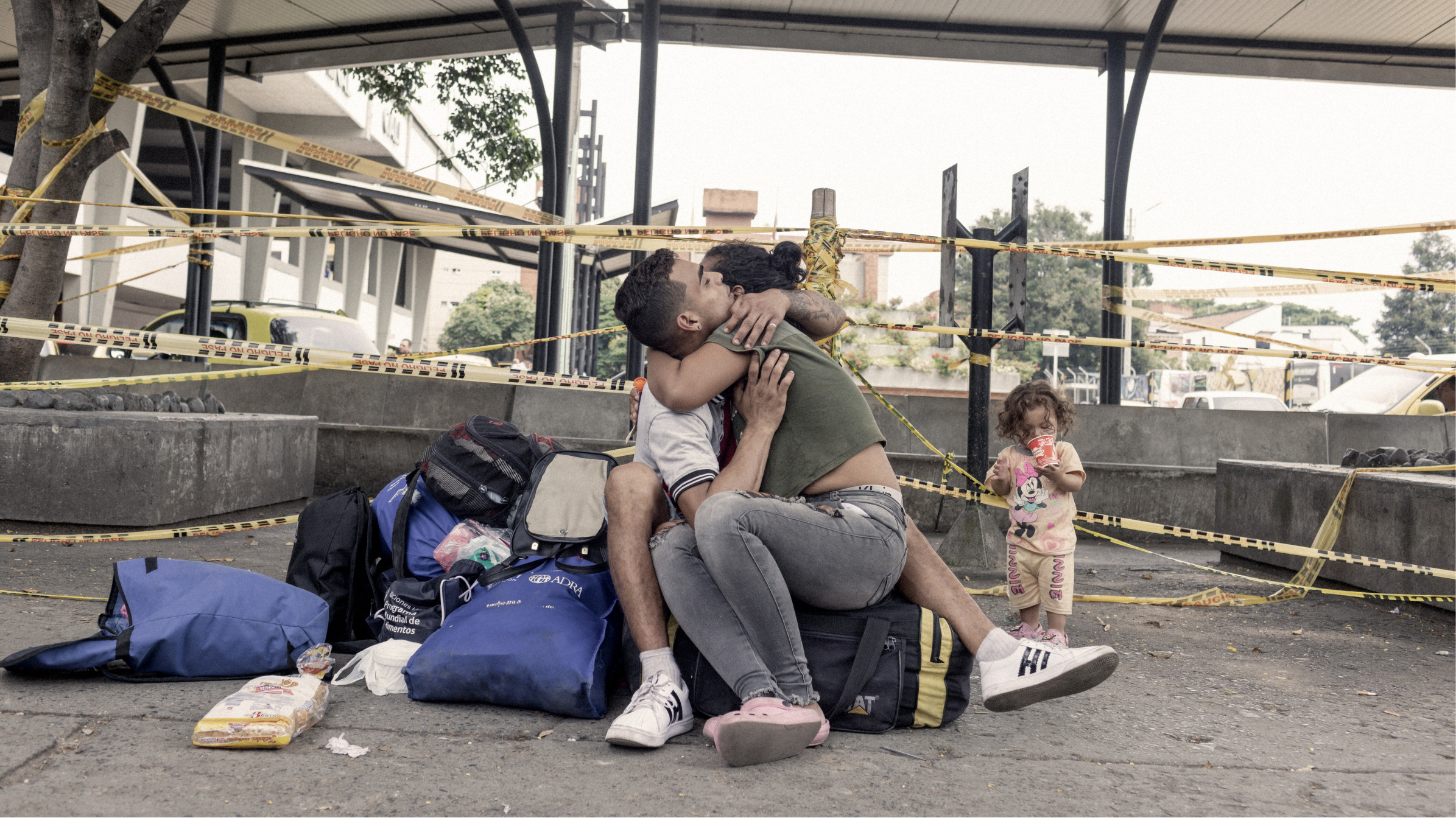 María Fernanda Artigas, de 22 años (centro, camiseta verde) abraza a su pareja, Endry Cordero Ávila, de 22 años, mientras su hija de 17 meses, Jerley, disfruta de una bebida fría en la terminal de autobuses de Cali, Colombia. La familia intenta regresar a su Venezuela natal tras varios años en el extranjero.